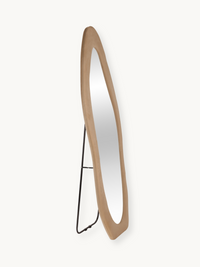 Angled side view of Seraphina floor mirror, taupe suede velvet oval frame and black metal stand on light background