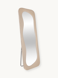Felis standing mirror in teddy white, angled three-quarter view showing wavy glass, bouclé frame texture, and black metal…