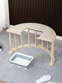 Natural wood semicircular climbing arch on grey striped rug, angled view showing spindle legs, with grey collapsible stora…