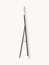 Side profile of white teddy fabric oval floor mirror on black metal easel stand, showing slim edge depth against plain bac…