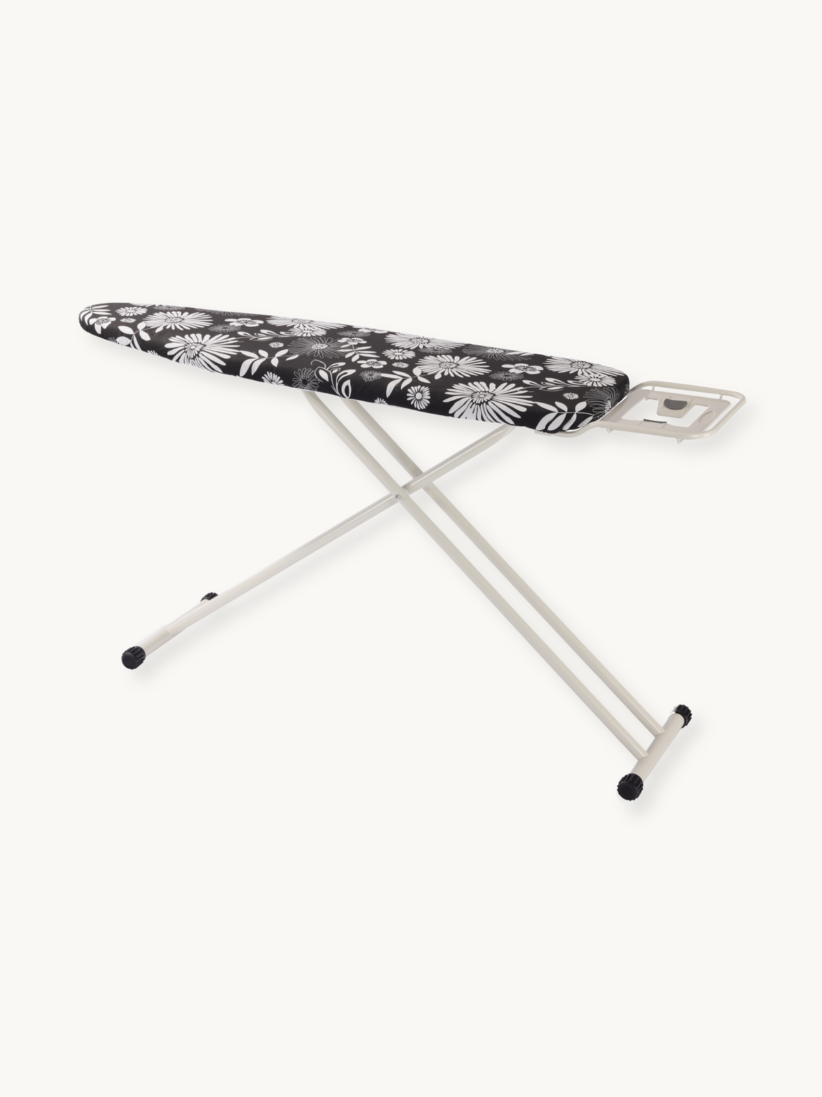 Angled front view of ironing board with black daisy-print cotton cover, cream steel X-frame legs, rubber feet, and iron rest
