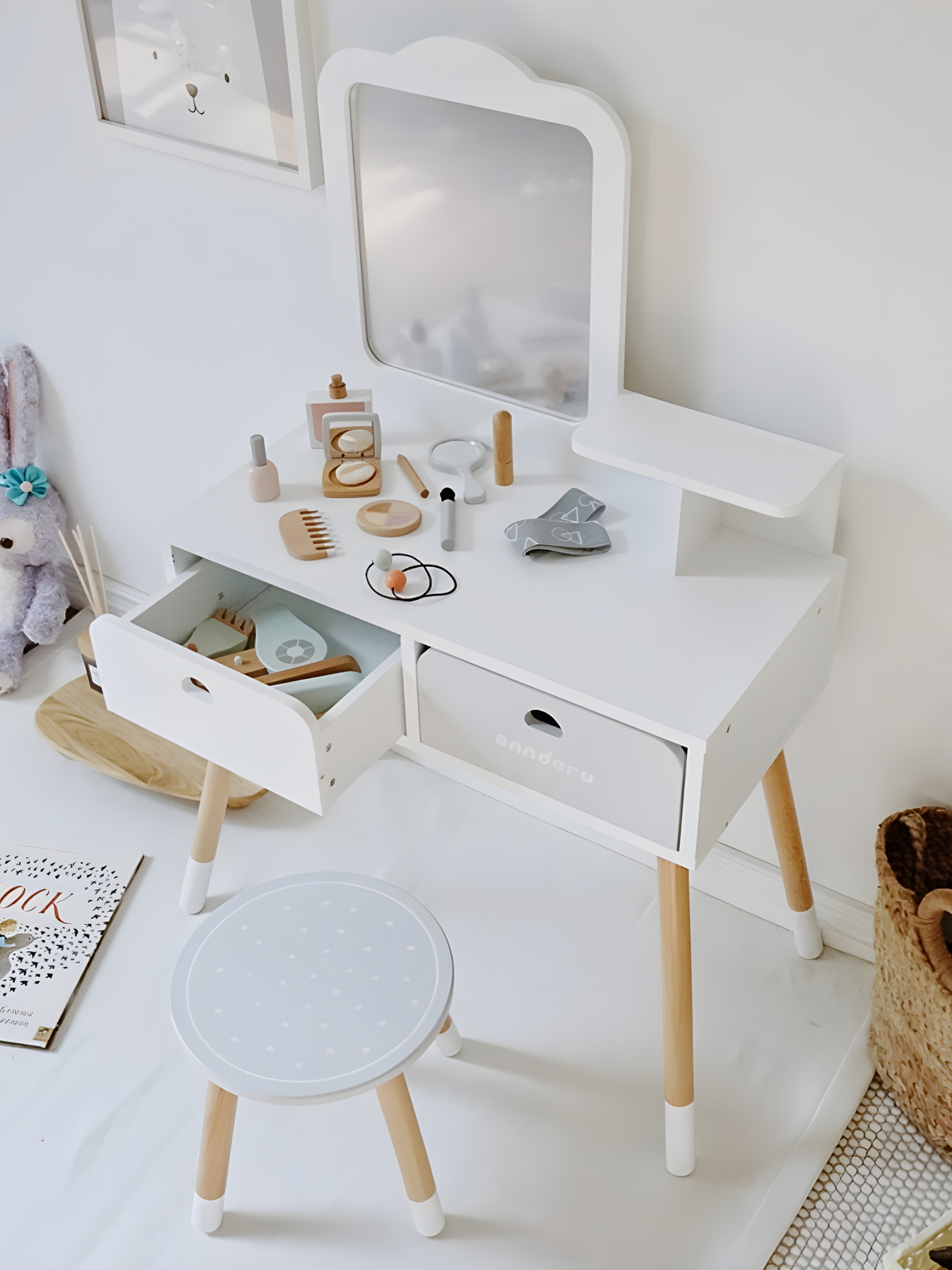 White children's vanity set from above, open drawer revealing toy accessories, stool with grey dotted seat, natural wood l…