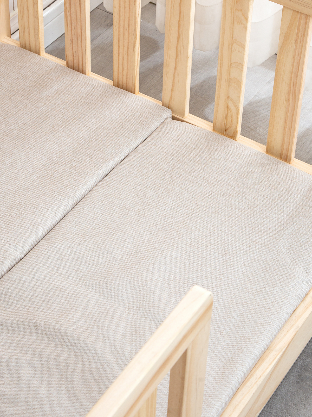 Close-up overhead detail of two beige cellucotton mattresses fitted side by side inside natural pine crib slats