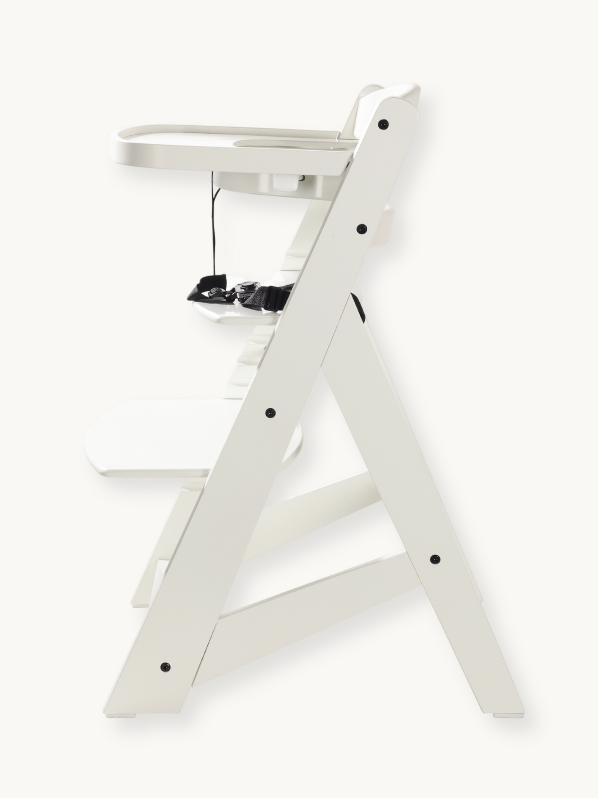 White wooden baby high chair side profile showing A-frame leg structure, attached tray, black safety harness, and black bo…