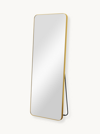 Tall rectangular full-length mirror with gold aluminium frame, angled three-quarter view showing black kickstand, white ba…