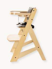 Natural wood highchair side profile showing A-frame legs, adjustable footrest shelf, grey seat cushion with harness, and a…