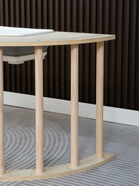Close-up of natural birch plywood tabletop edge and four turned spindle legs on grey striped rug, dark slatted wall behind