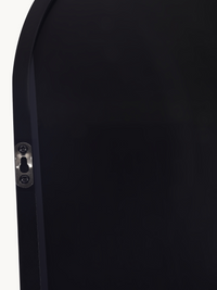 Close-up of black aluminium oval mirror frame edge showing silver keyhole wall-mount bracket with screws