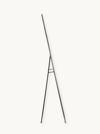 Side profile of taupe aluminium arched mirror showing slim frame and black metal easel stand legs, white background