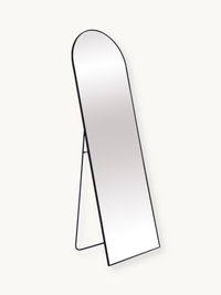 Arched full-length freestanding mirror with thin black aluminium frame, angled three-quarter view on light background