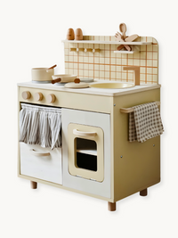 Cream and white wooden toy kitchen with oven, sink, hob knobs, tiled backsplash, and wooden utensils, shown at a front angle