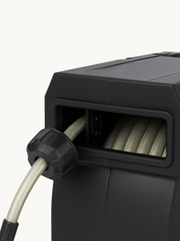 Close-up of black plastic hose reel casing showing braided grey hose coiled on internal drum through open front slot, with…