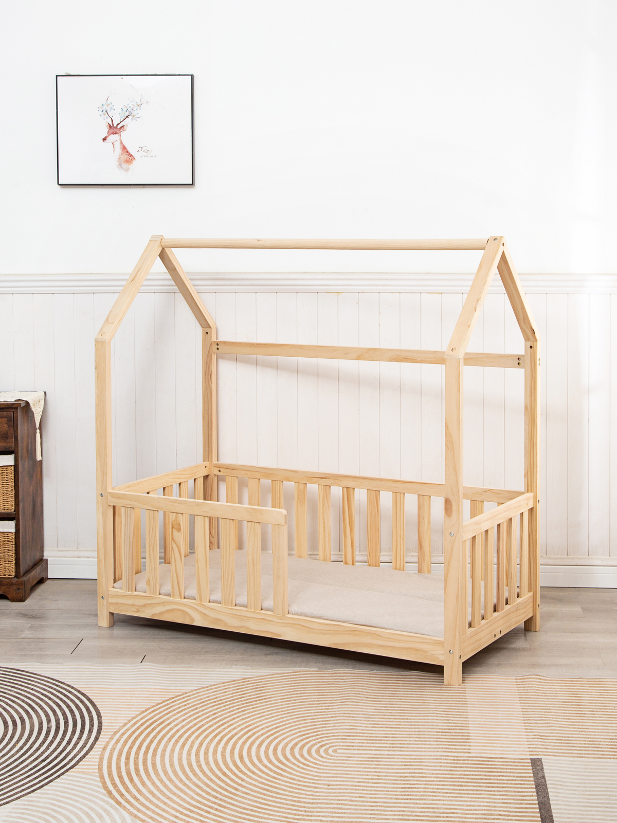 Natural pine toddler house bed with roof frame and spindle safety rails, front view in styled nursery room with patterned rug