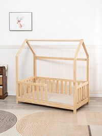 Natural pine toddler house bed with roof frame and spindle safety rails, front view in styled nursery room with patterned rug