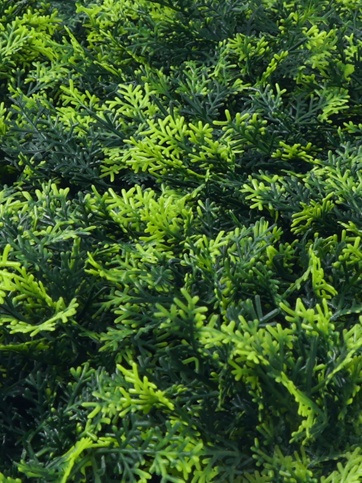 Close-up detail of artificial olive green hedge panel showing mixed bright and dark green plastic foliage texture