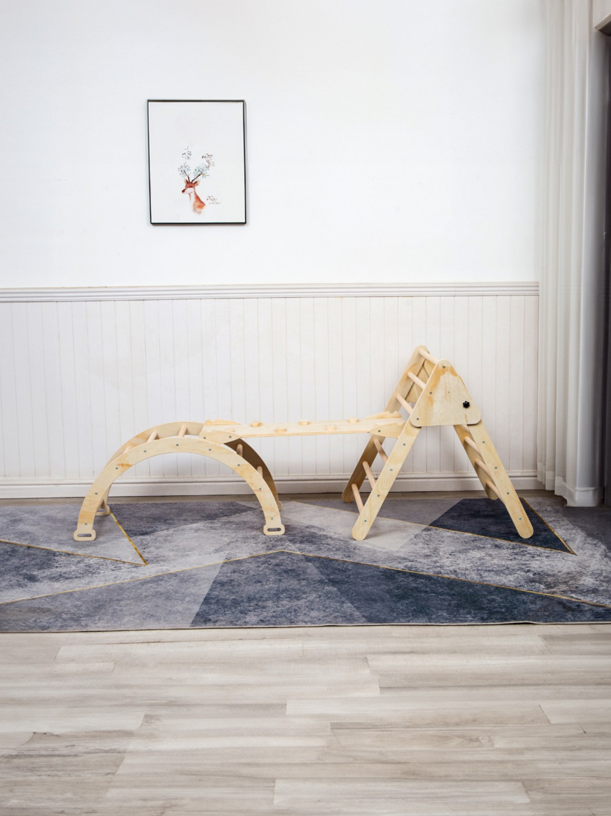 Natural wood climbing triangle connected to arch rocker and ramp on grey geometric rug, side view in bright playroom, no c…