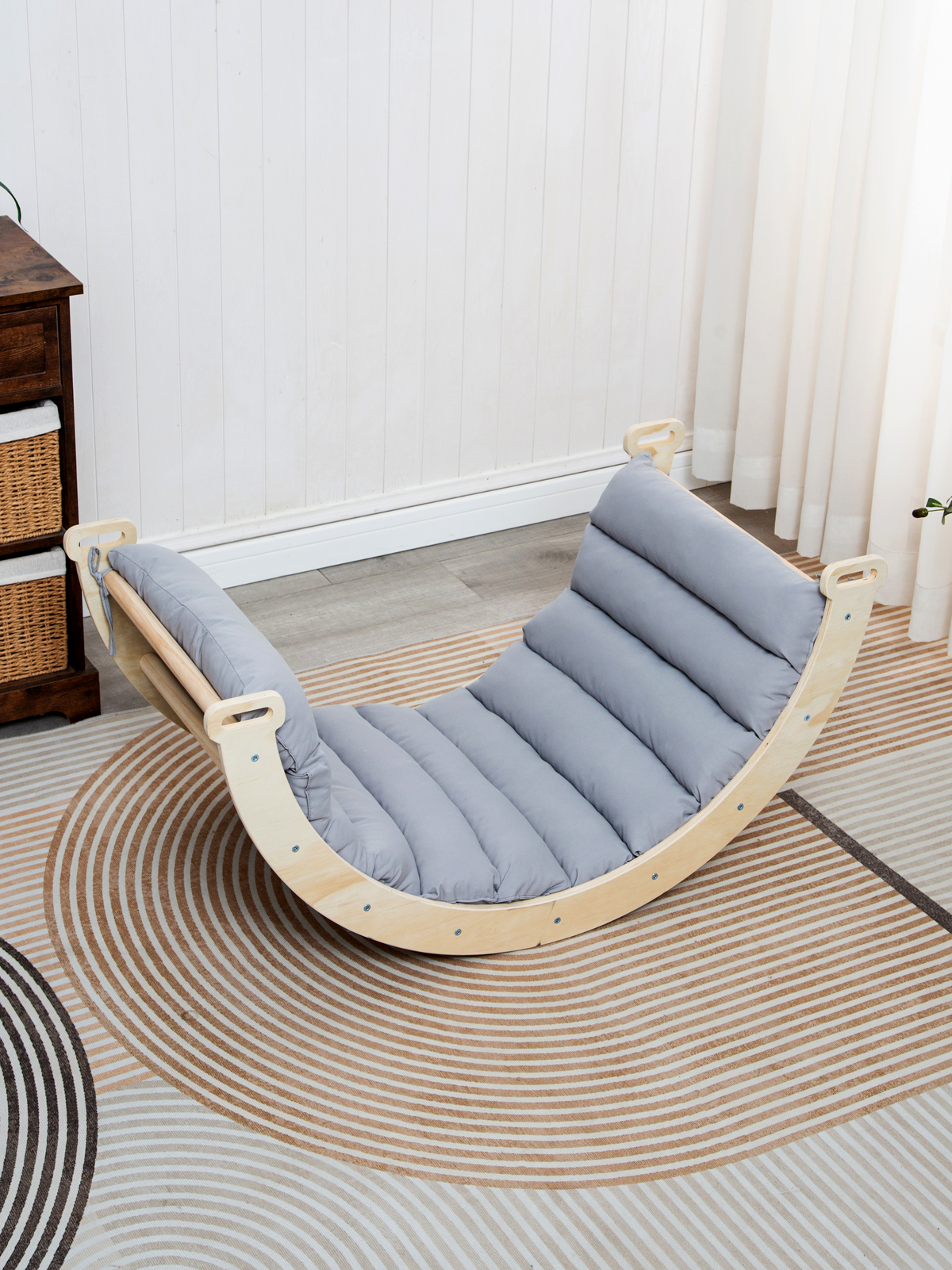 Grey quilted cushion fitted on natural wood climbing arch, angled front view on striped rug, bright room with curtains