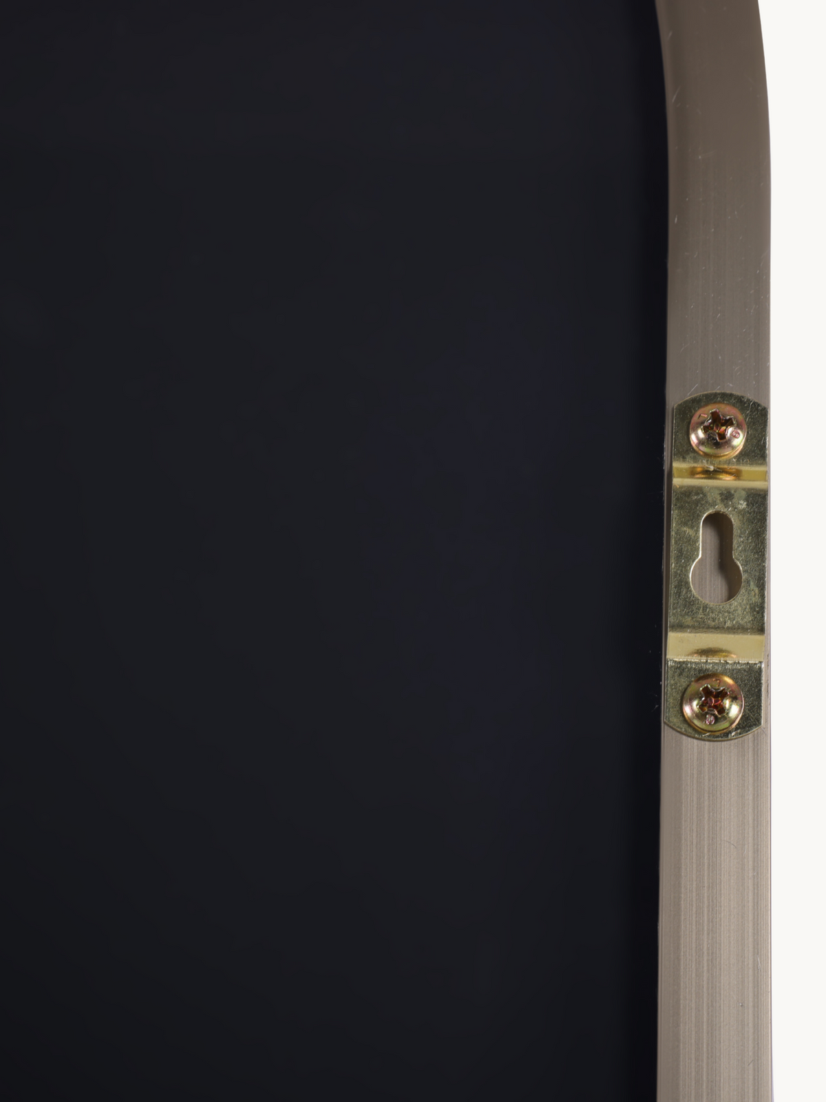 Close-up of gold-tone keyhole wall-mounting bracket screwed onto the back of a taupe brushed aluminium mirror frame