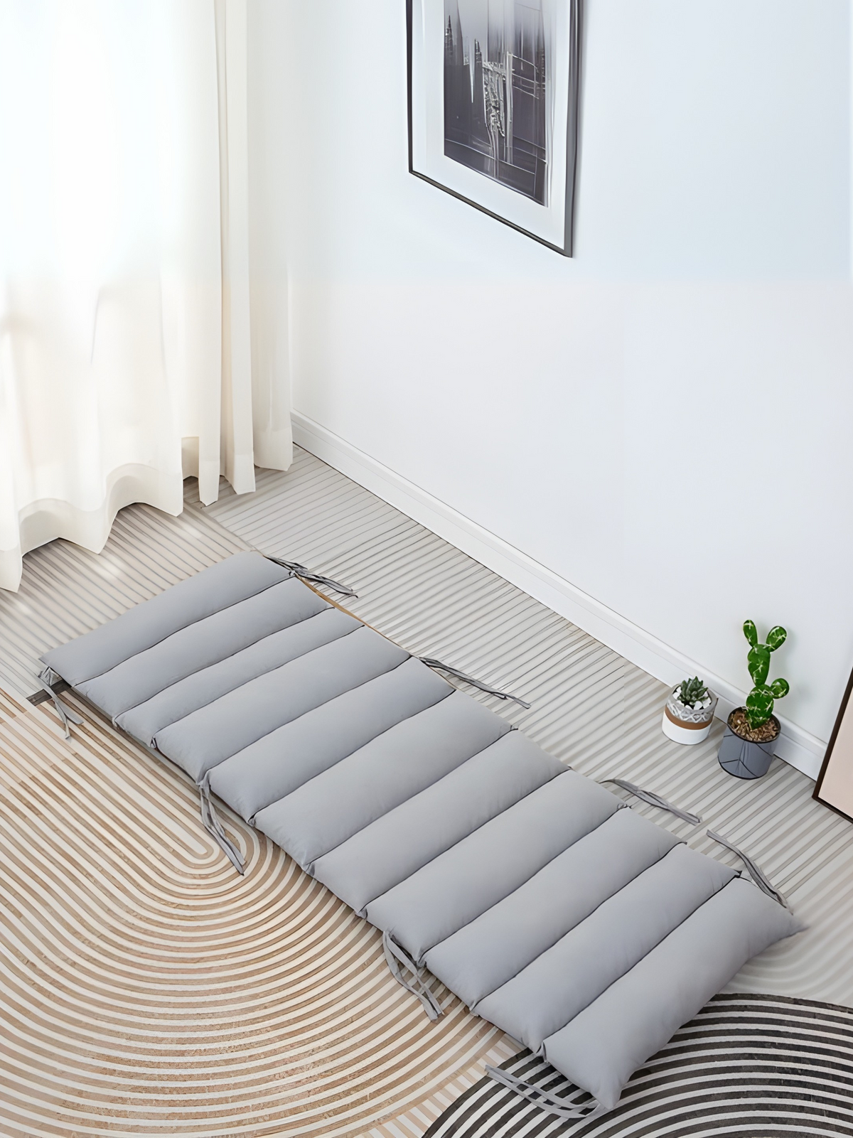 Grey quilted climbing arch cushion laid flat on a patterned rug in a bright room, overhead angle, tie strings visible