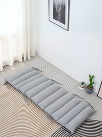 Grey quilted climbing arch cushion laid flat on a patterned rug in a bright room, overhead angle, tie strings visible
