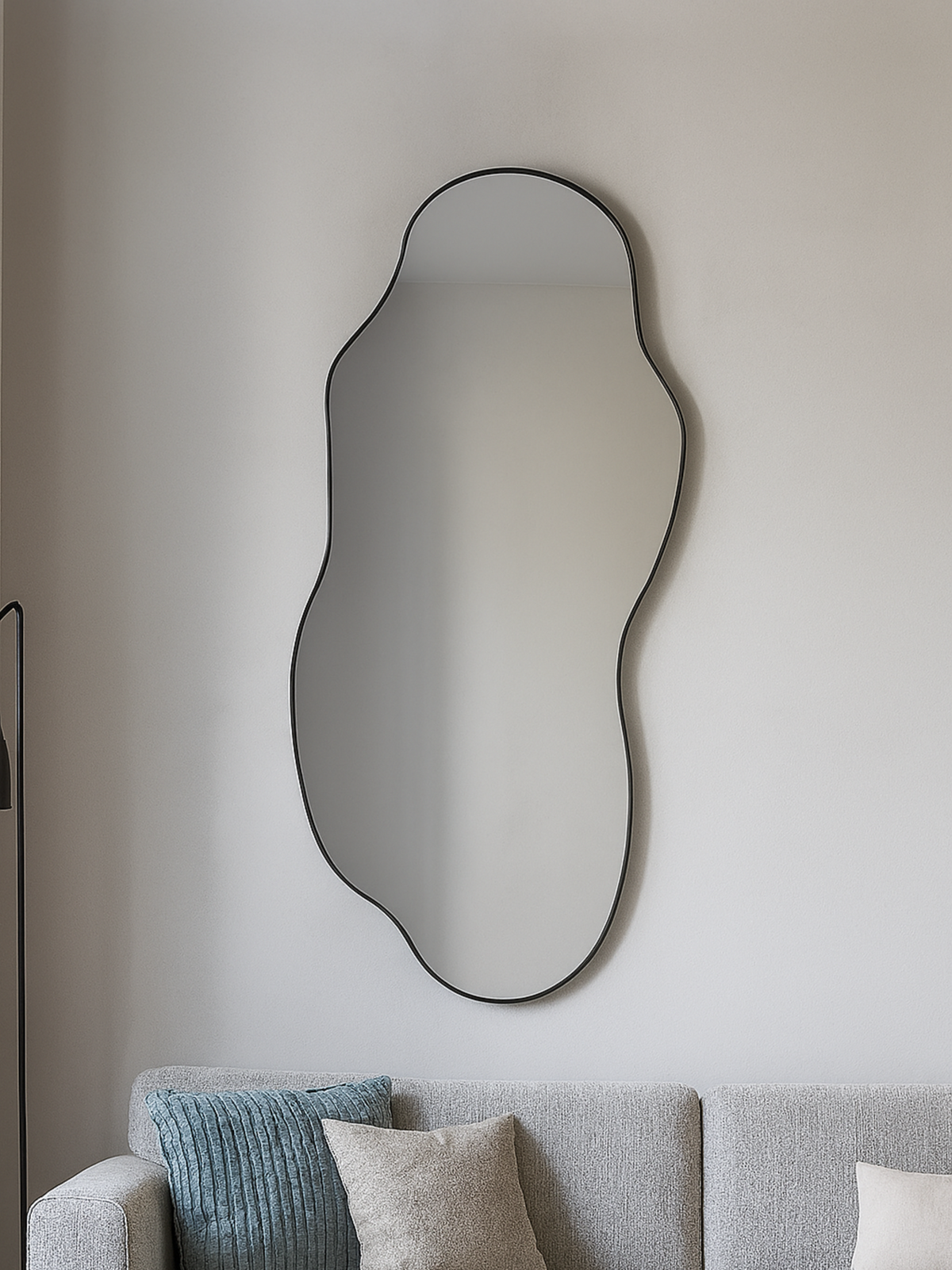 Luciano organic mirror with thin black PVC frame hung above a grey sofa with blue and beige cushions, lifestyle room view