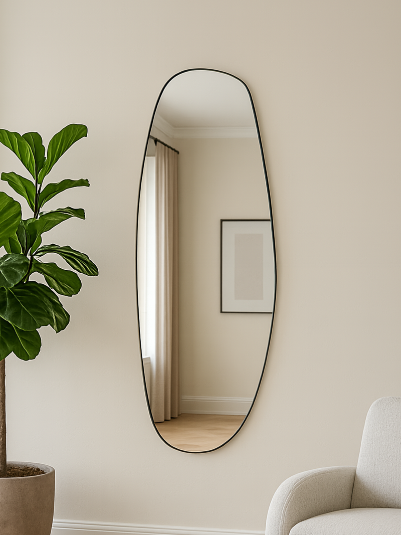 Tall oval Rafael mirror with thin black frame hung on cream wall beside fiddle-leaf fig plant and cream armchair