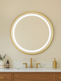 Round gold-framed LED mirror glowing with bright ring light, mounted above marble vanity with brass faucets, front lifesty…