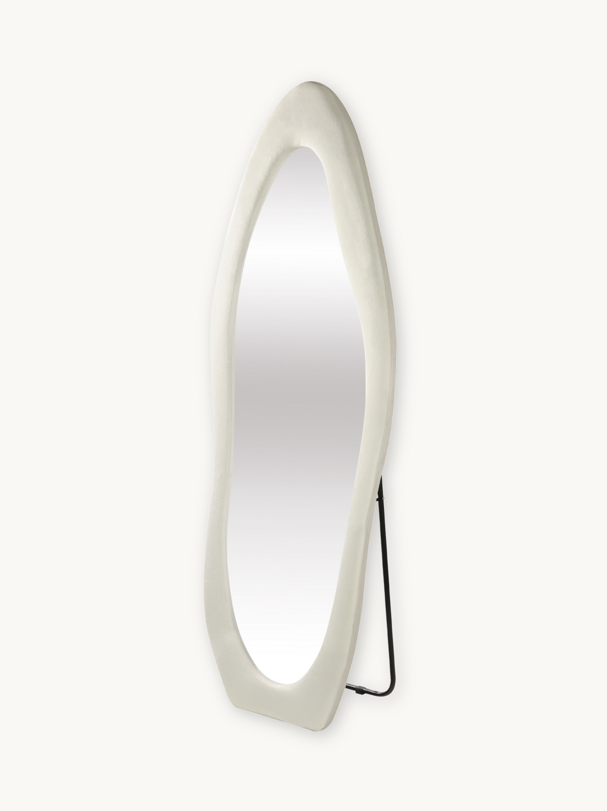 Angled three-quarter view of tall oval standing mirror with chunky white suede velvet frame and black metal easel back stand