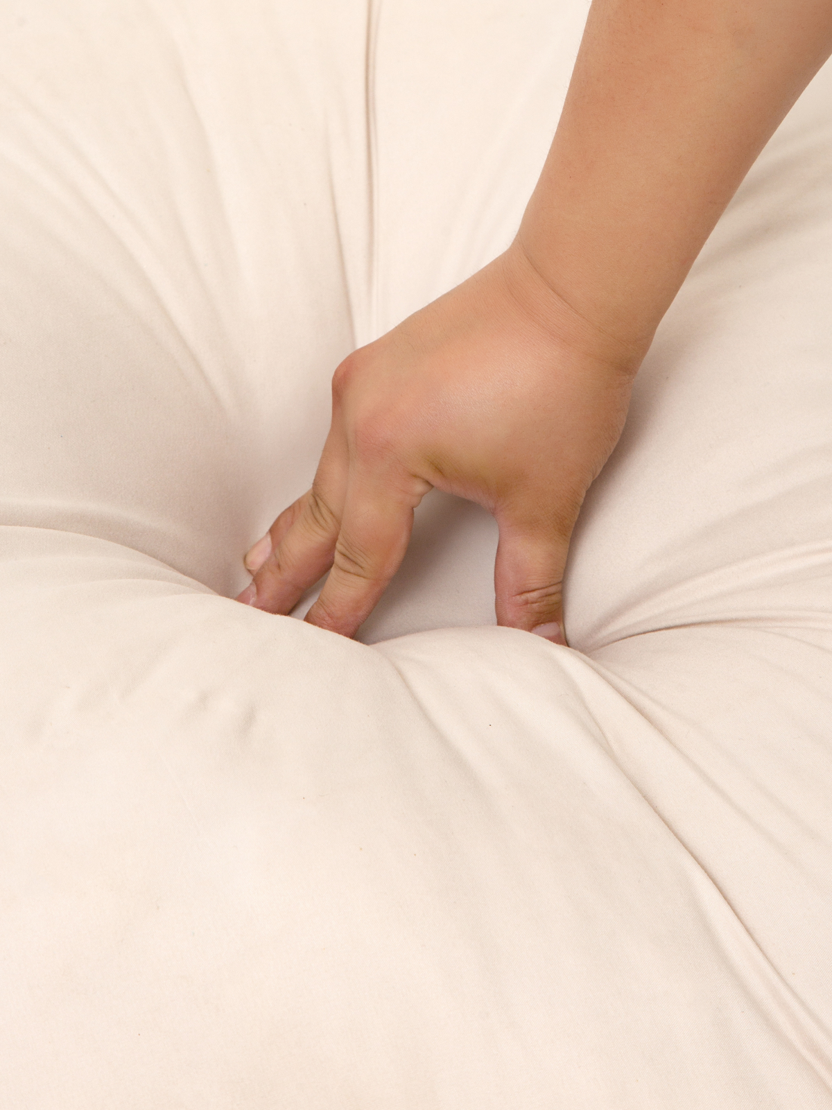 Hand pressing fingers into cream white floor cushion surface, showing soft give and plush cellulose cotton fill depth