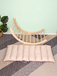 Natural wood climbing arch rocker leaning against mint wall, blush pink segmented cushion laid flat on patterned floor, mo…