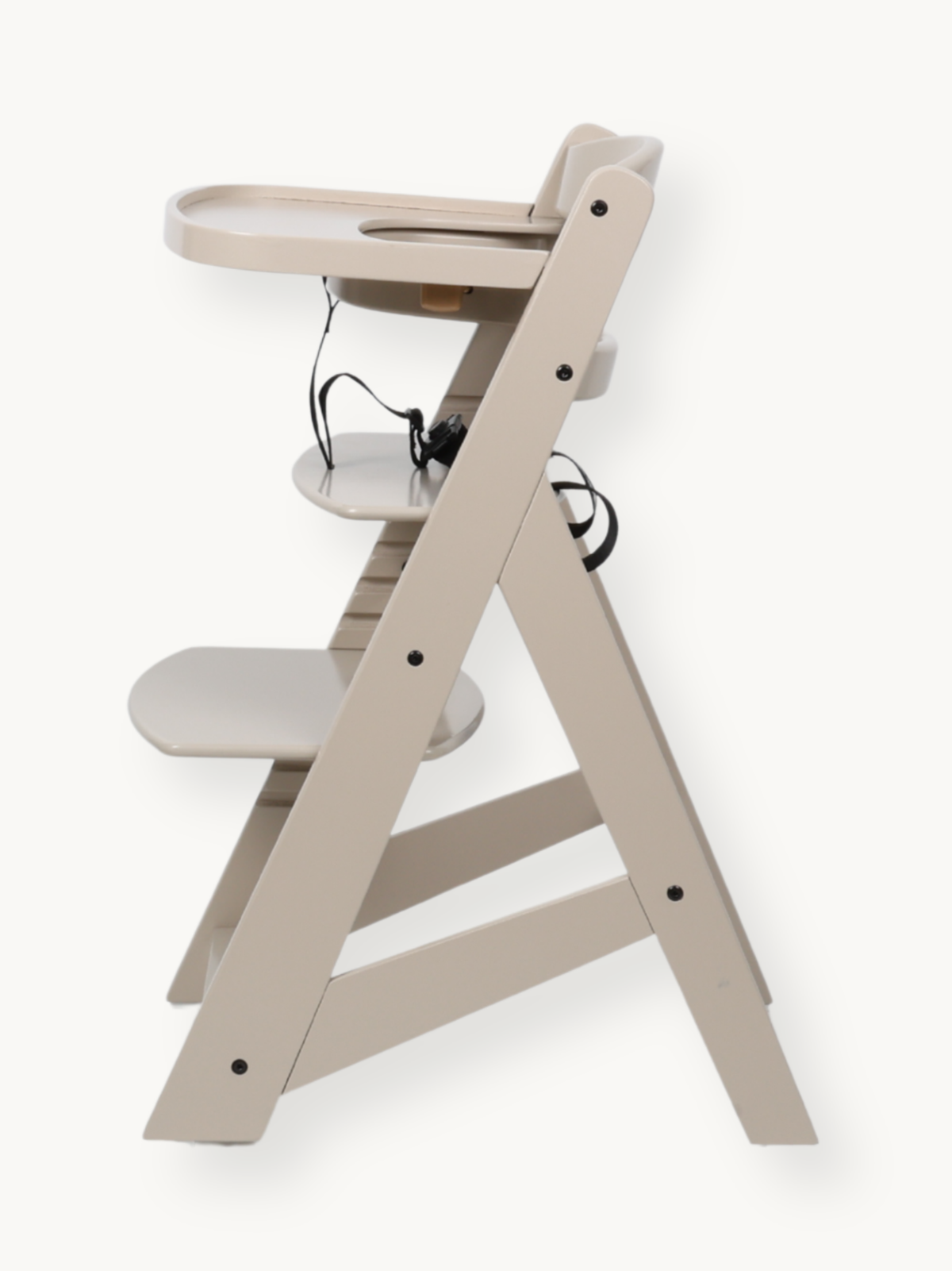 Side profile of clay beige wooden highchair with attached tray, adjustable footrest, and black safety harness straps visible