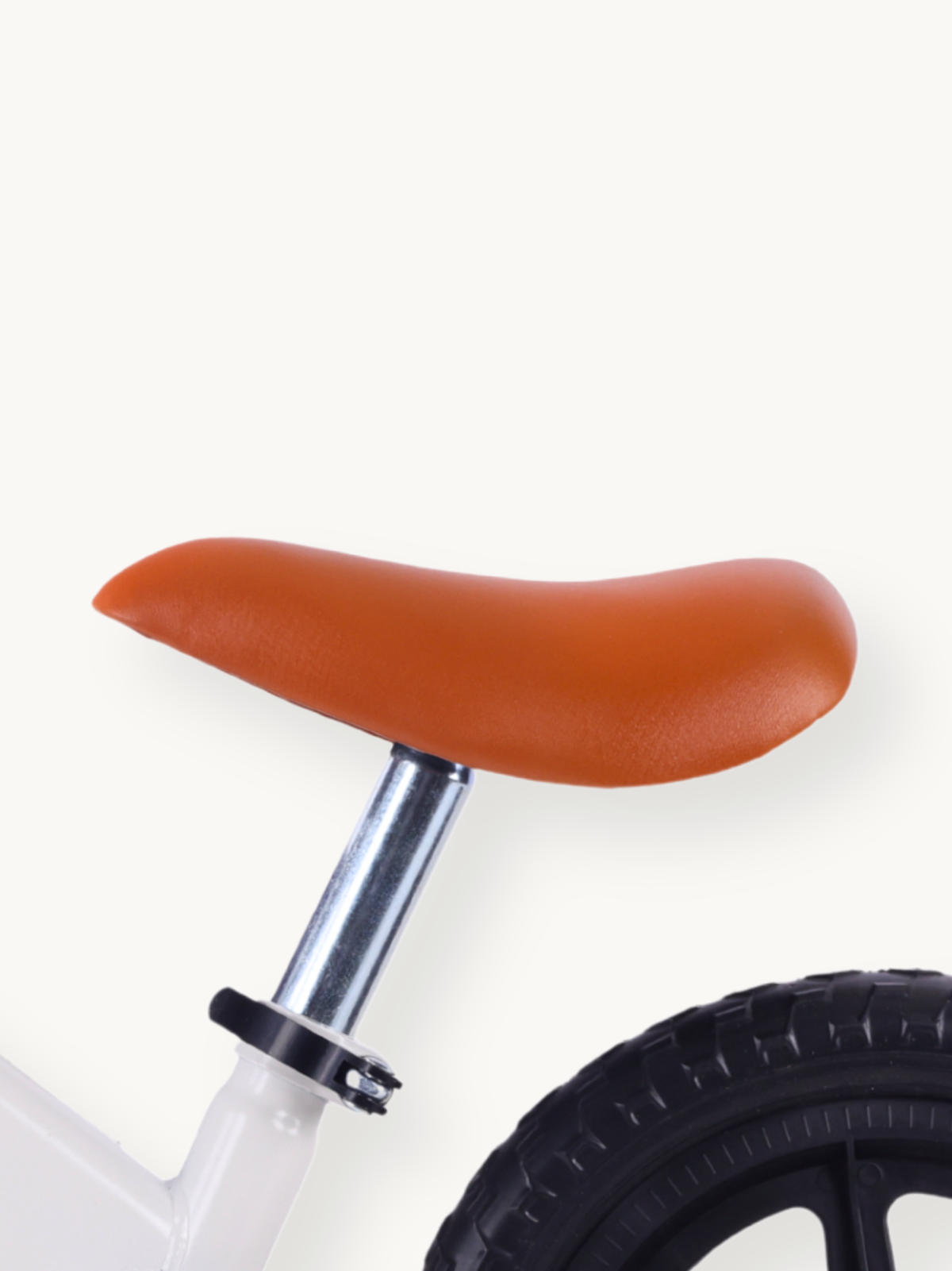 Close-up of tan leather-look saddle on chrome seatpost, white steel frame and partial black rubber rear tire visible