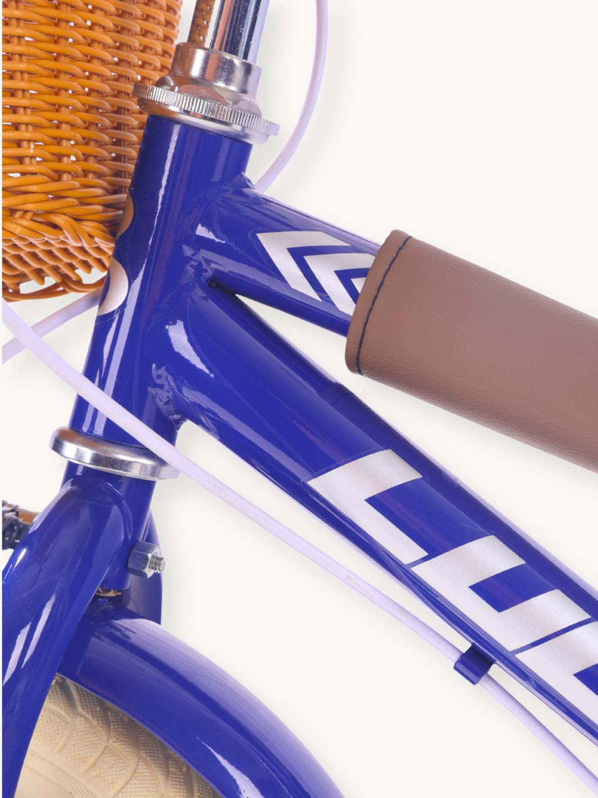Close-up of dark blue carbon-steel frame junction with white chevron graphics, brown handlebar grip, and wicker basket edg…