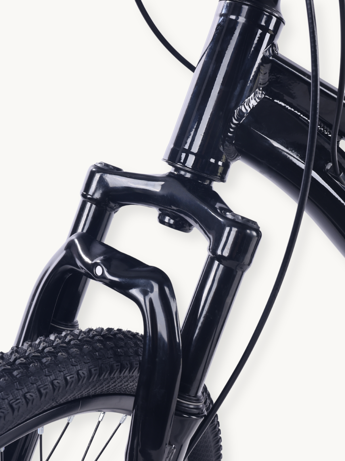 Close-up of gloss black front suspension fork and knobby tyre on 20-inch kids' mountain bike, showing crown, stanchions an…