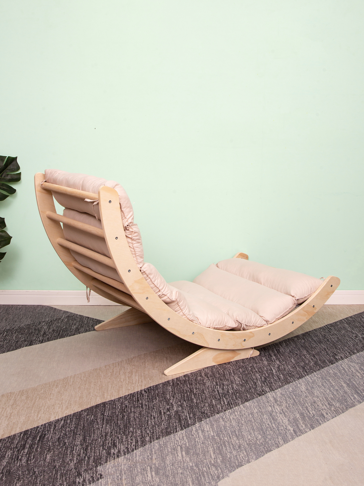 Angled side view of natural wood climbing arch rocker with blush pink quilted cushion attached, on striped carpet against…