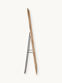 Rear view of wavy full-length mirror showing natural wood frame back and black metal easel stand, side profile angle