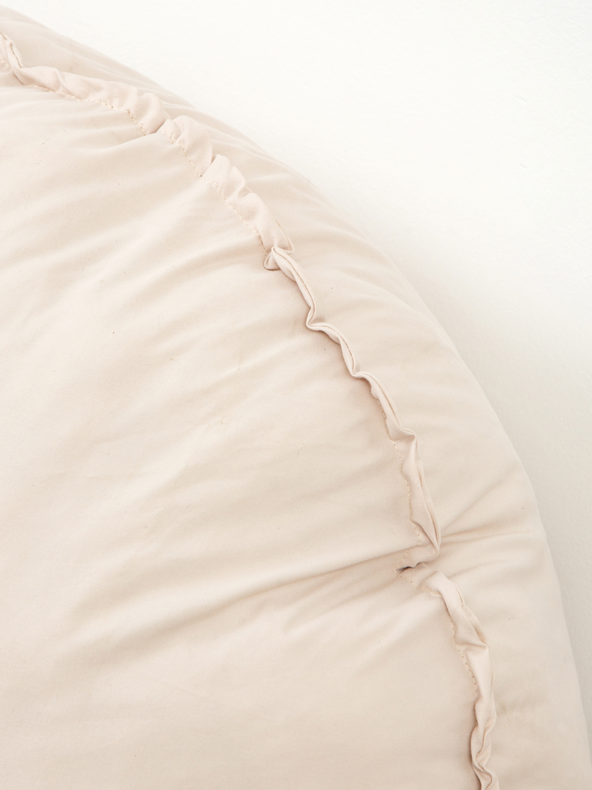 Close-up of cream white floor cushion corner showing scalloped seam stitching and smooth fabric surface texture