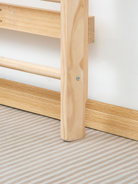 Close-up of natural wood climbing frame leg and base rail on striped beige floor, showing screw fixing detail against whit…