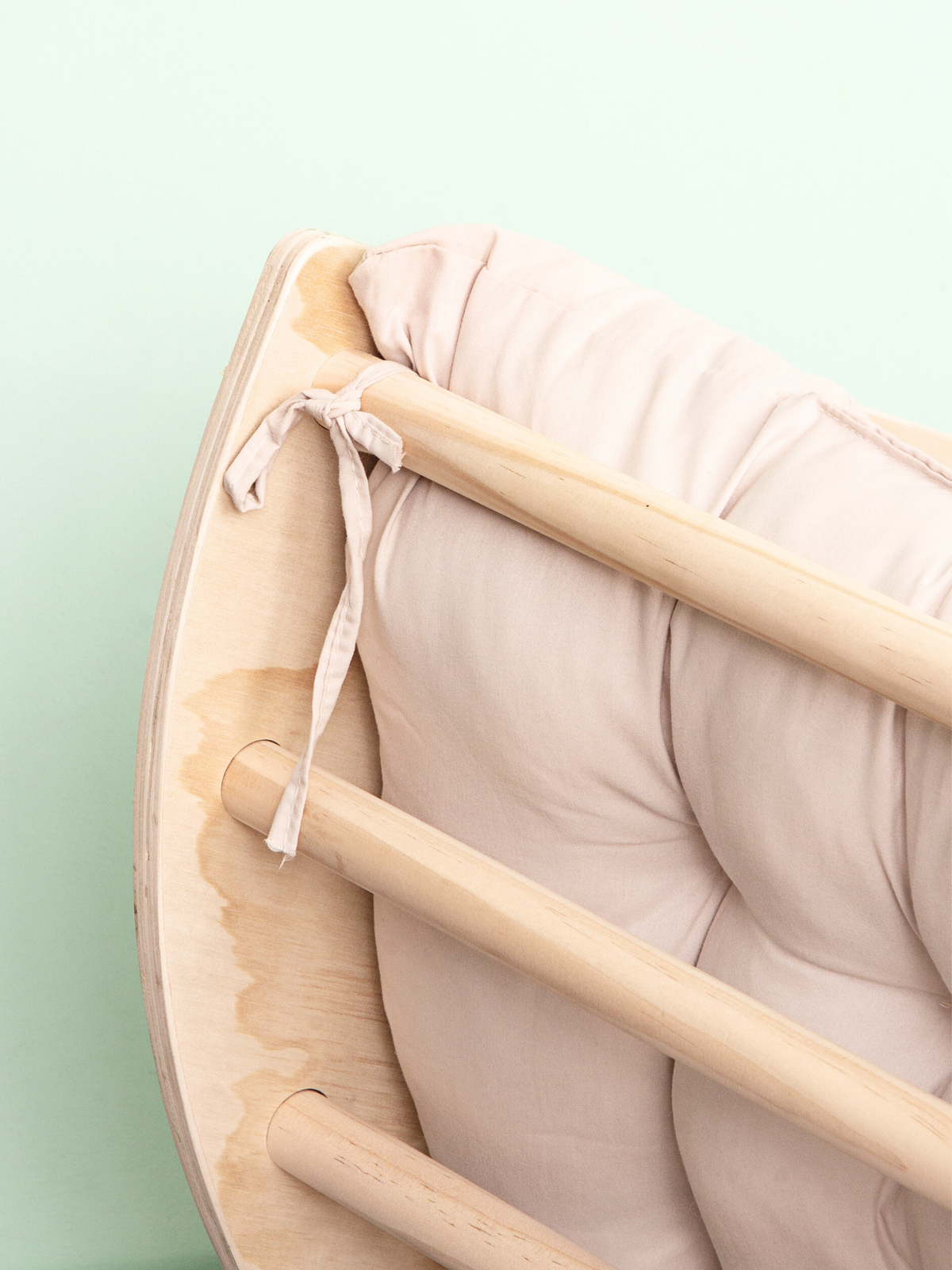 Close-up of blush pink cushion tied to natural birch wood rails of climbing arch, showing fabric tie detail against mint b…