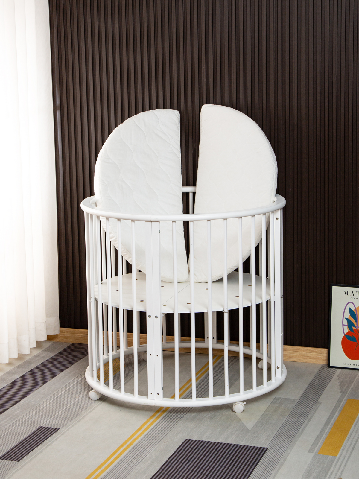 White round wooden playpen on casters with split circular mattress standing upright inside, angled rear view in styled nur…