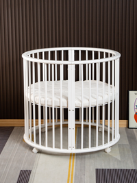 White round wooden playpen with vertical slats and quilted circular mattress on casters, front angle, styled in modern roo…