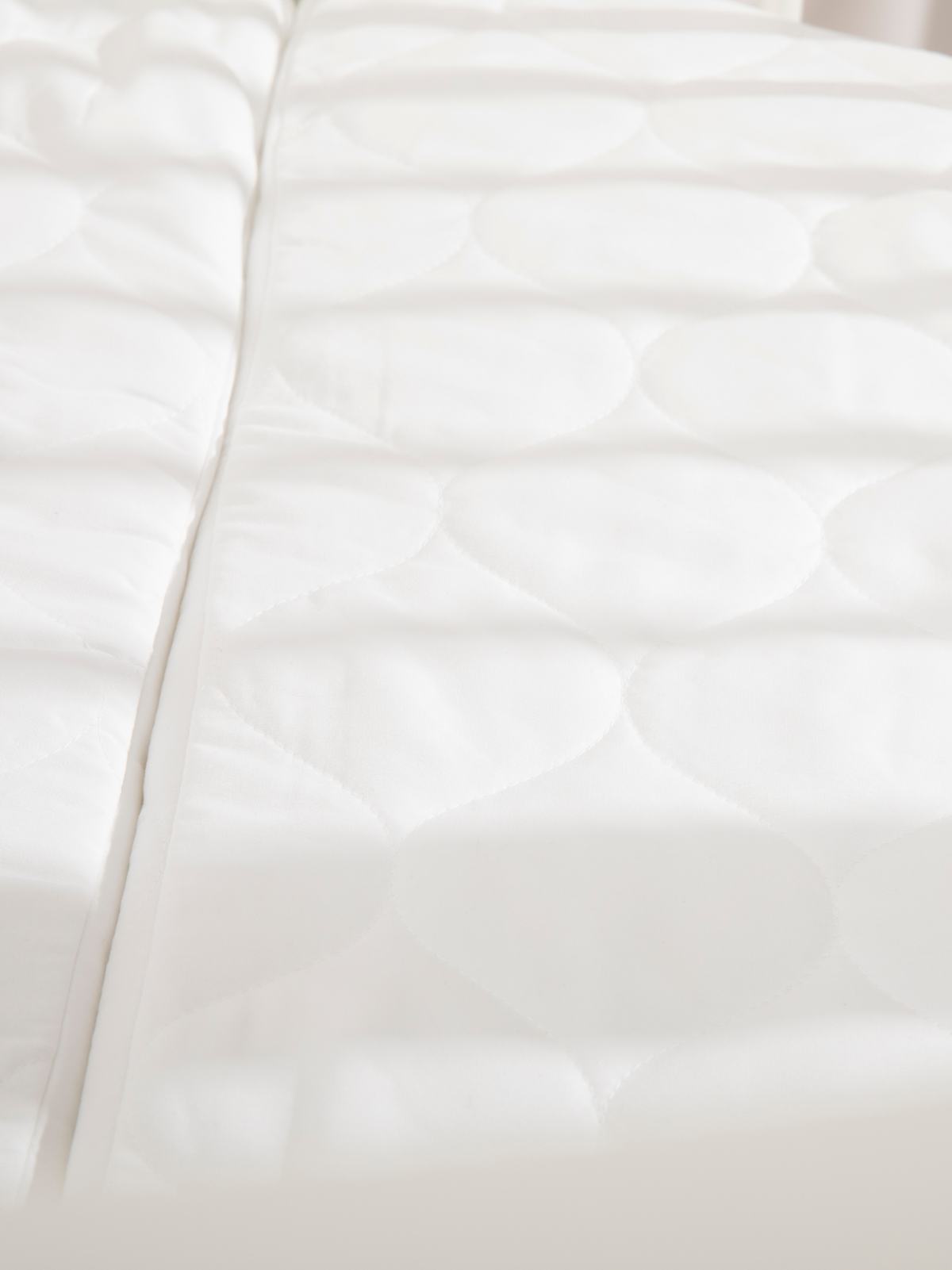 Close-up of white quilted oval mattress surface showing circular stitched pattern, included with round playpen