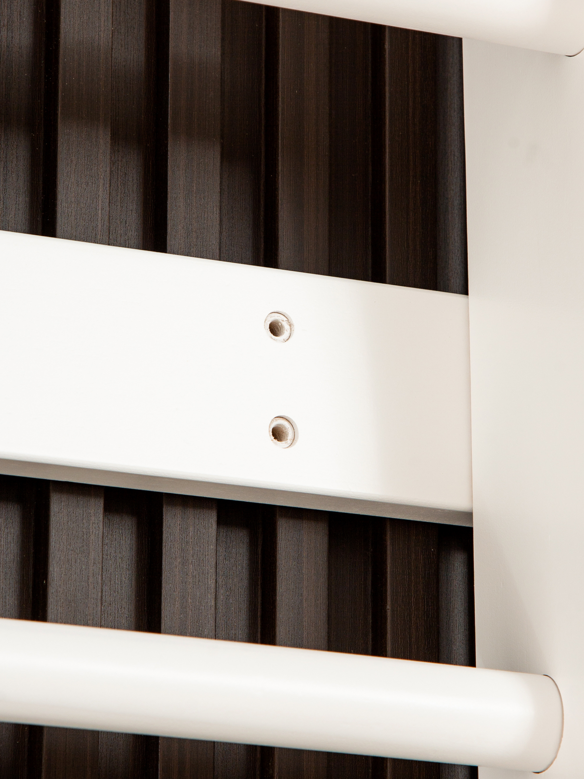 Close-up of white climbing frame bracket with two metal screw holes, mounted against dark wood slatted wall panel