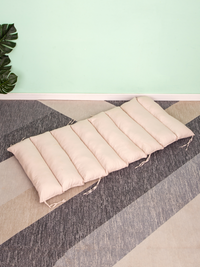 Cream quilted cushion laid flat on striped carpet, showing channel stitching and fabric ties along the sides, mint wall be…