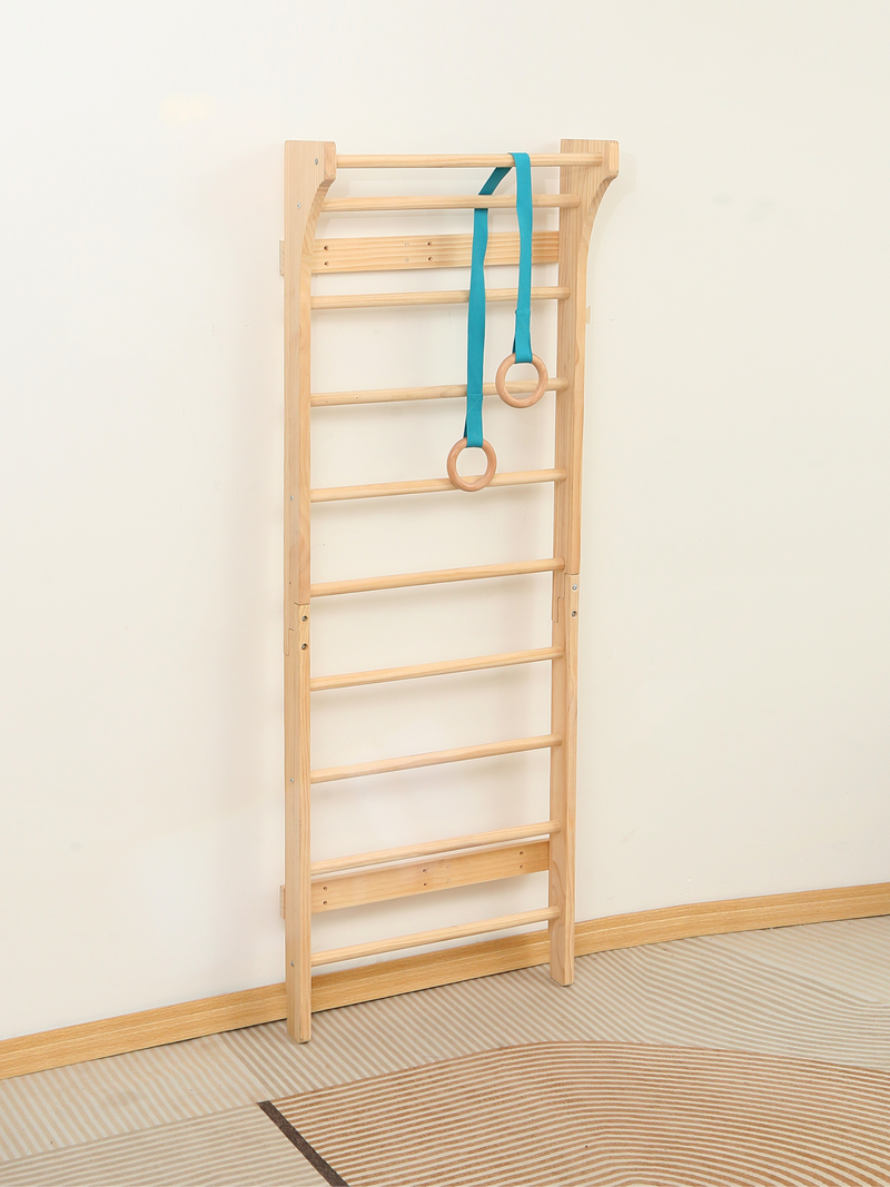 Natural wood wall bar ladder leaning against white wall with teal gymnastic rings attached, full-length side angle on stri…