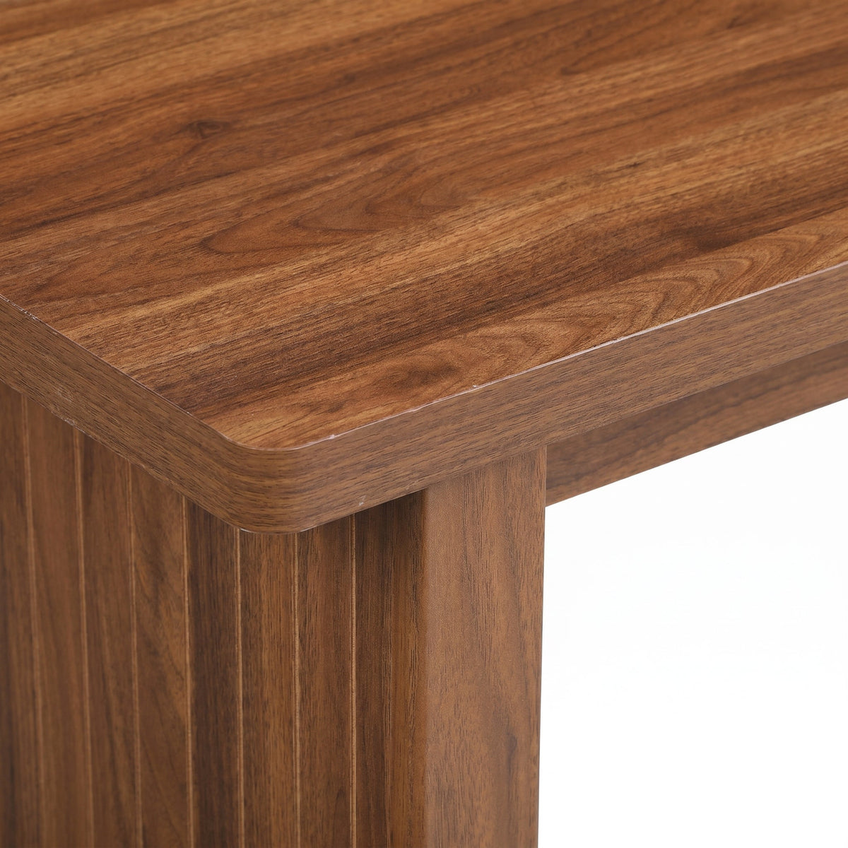 Close-up of walnut-finish tabletop corner showing smooth rounded edge and natural wood grain above a ribbed leg detail