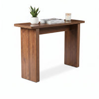 Walnut console table angled view styled with snake plant, stacked magazines, and lit candle on top, white background