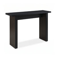 Black console table with vertical ribbed leg panels revealing warm wood grain, flat top, angled three-quarter view on whit…