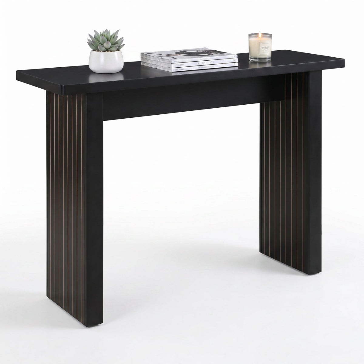 Black console table with fluted panel legs, styled with succulent, stacked magazines, and lit candle, three-quarter front…