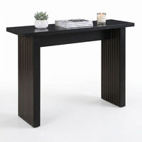 Black console table with fluted panel legs, styled with succulent, stacked magazines, and lit candle, three-quarter front…